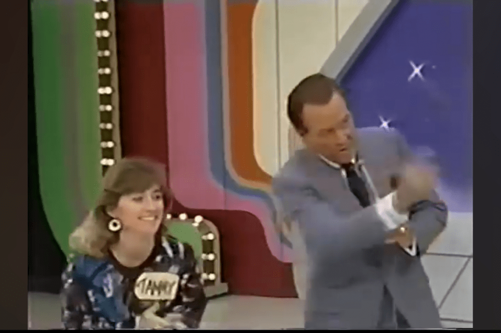 A contestant named Tammy smiles as she participates in a game show, while the host gestures animatedly, surrounded by a colorful game show set.