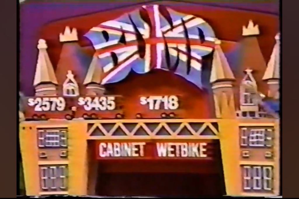 Colorful game show display featuring prices for items: 79, 35, and 18, with a sign reading 'CABINET WETBIKE' and decorative towers in the background.