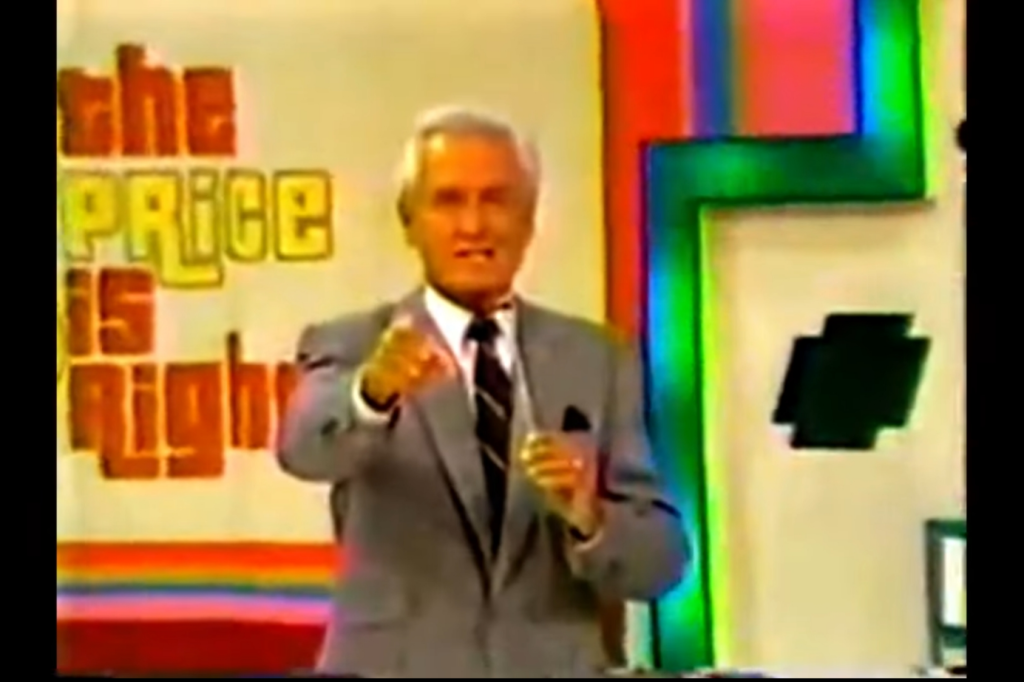 A host stands in front of a colorful backdrop featuring the show's title 'The Price is Right,' gesturing and engaging with the audience.
