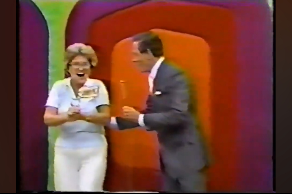 A woman joyfully celebrates while holding a prize as a man in a suit stands beside her, surrounded by colorful background panels.