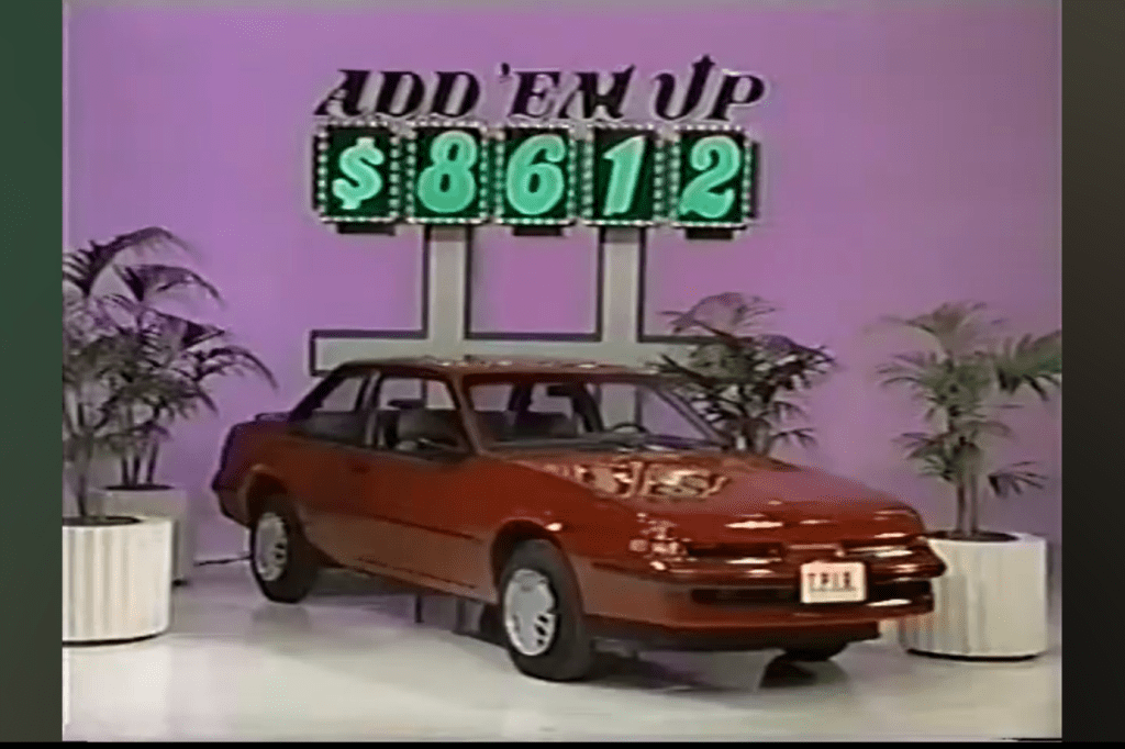 A red car is displayed with the game 'Add 'Em Up' signage showing a price of 12 in a game show setting.