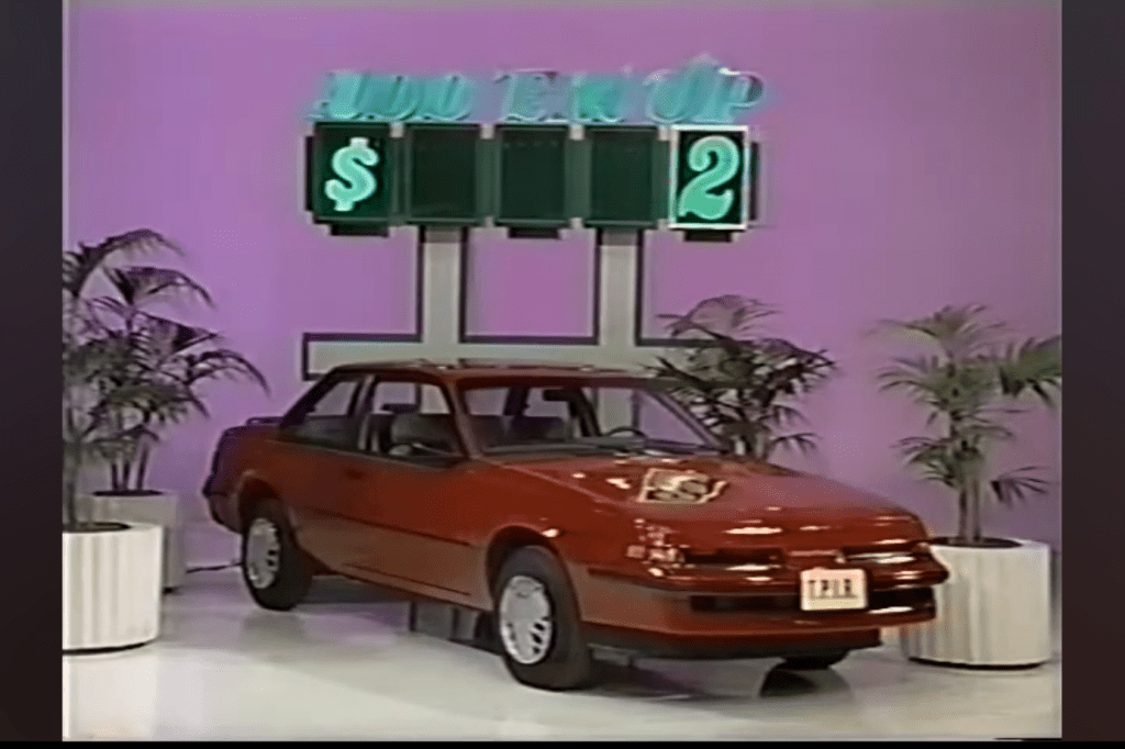 A red Pontiac Sunbird Coupe displayed under a neon sign reading 'ADD 'EM UP' with prices indicated.