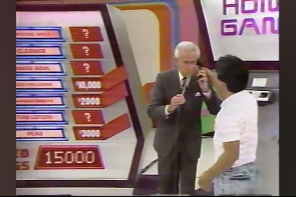 A contestant on 'The Price is Right' participating in 'The Phone Home Game,' with grocery items listed on a board and the host speaking to the at-home contestant on the phone.