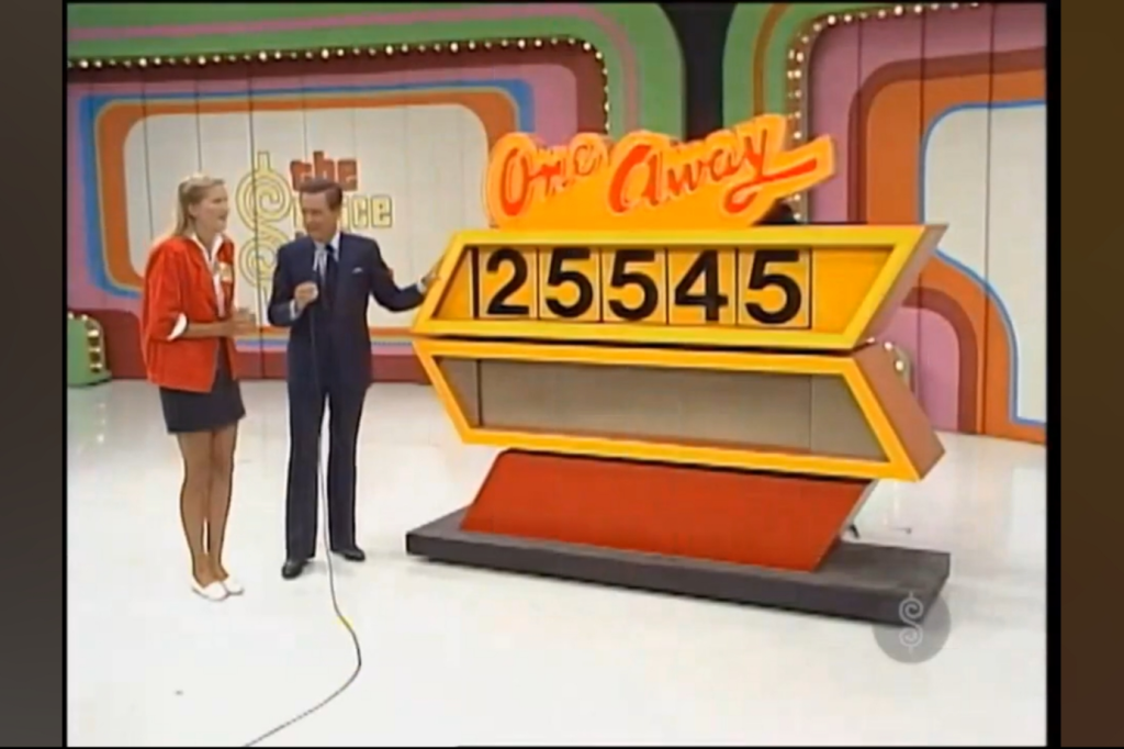A contestant and host interact on stage during the game 'One Away,' with a display showing the price '25545' on a large board.