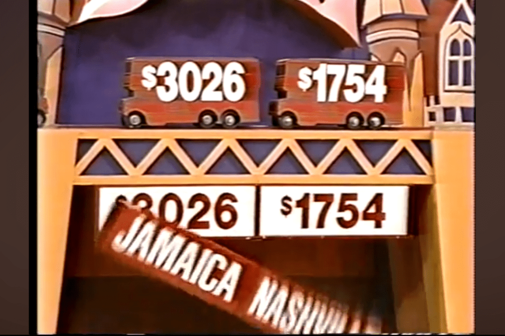 Two toy trucks displaying dollar amounts 26 and 54 on a game show set, with a sign showing 'JAMAICA NASHVILLE' falling beneath.