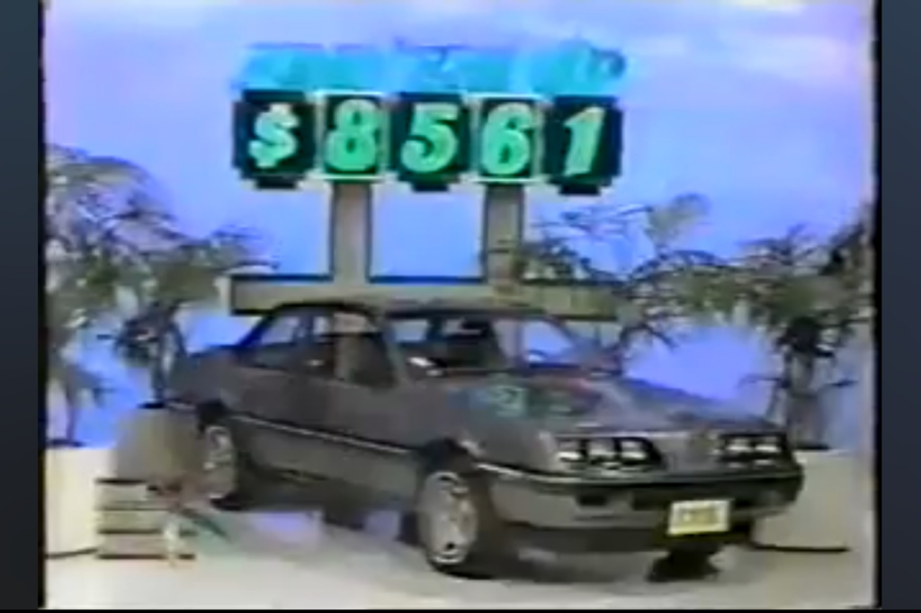 A gray Pontiac Sunbird Coupe displayed with a price tag of ,561 in a game show setting.