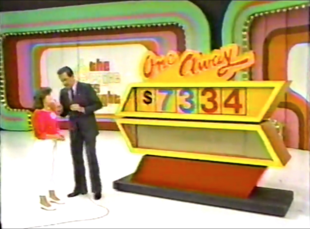 A contestant on The Price is Right stands next to the game's One Away display showing a price of ,334, while the host engages with her.