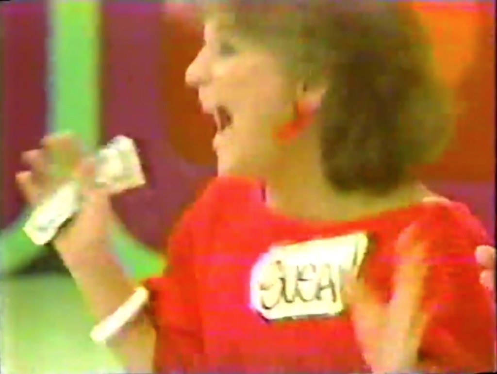 A contestant in a red shirt excitedly holds cash, celebrating a potential win on The Price is Right game show.