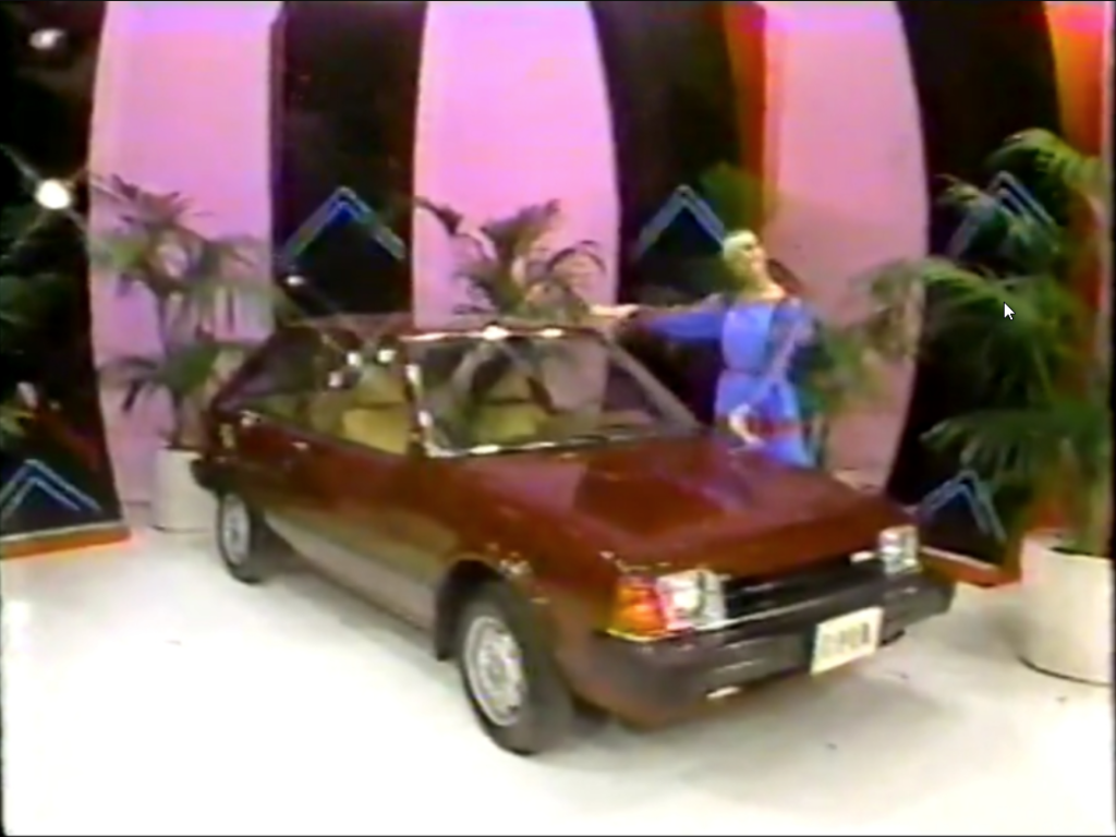 A model stands next to a red Mazda Hatchback car showcased in a colorful studio with pink and black backdrop, highlighting the vehicle's features.