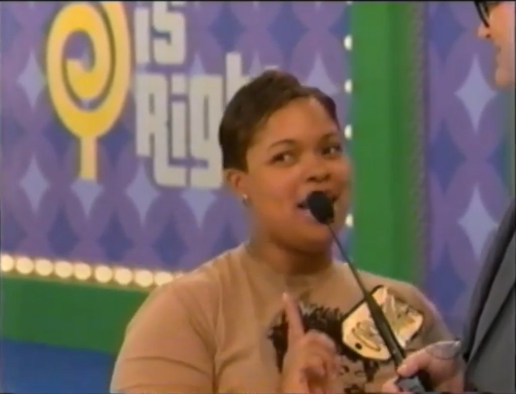 A contestant smiles while speaking into a microphone during a game show, with the 'The Price is Right' logo visible in the background.