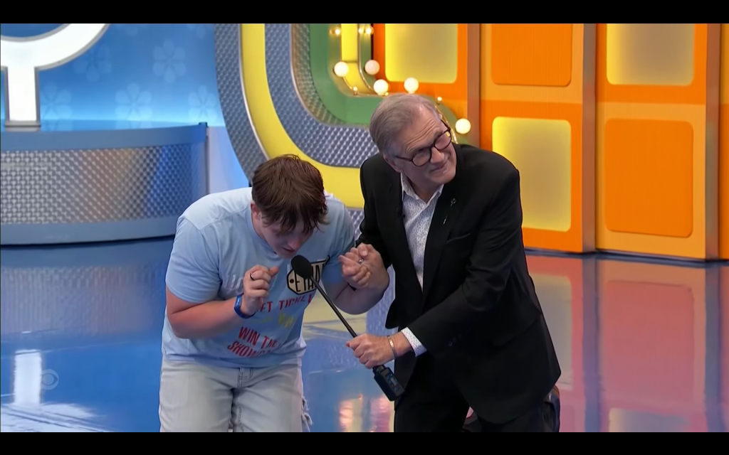 A contestant leans forward while holding a microphone, accompanied by a host who is smiling and engaging with the audience.