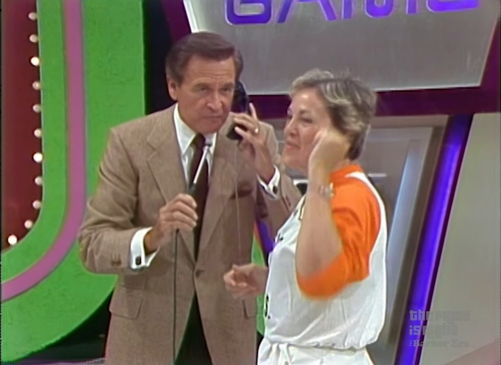 A contestant on stage participates in The Phone Home Game, speaking on a telephone while interacting with the host, who is standing nearby.
