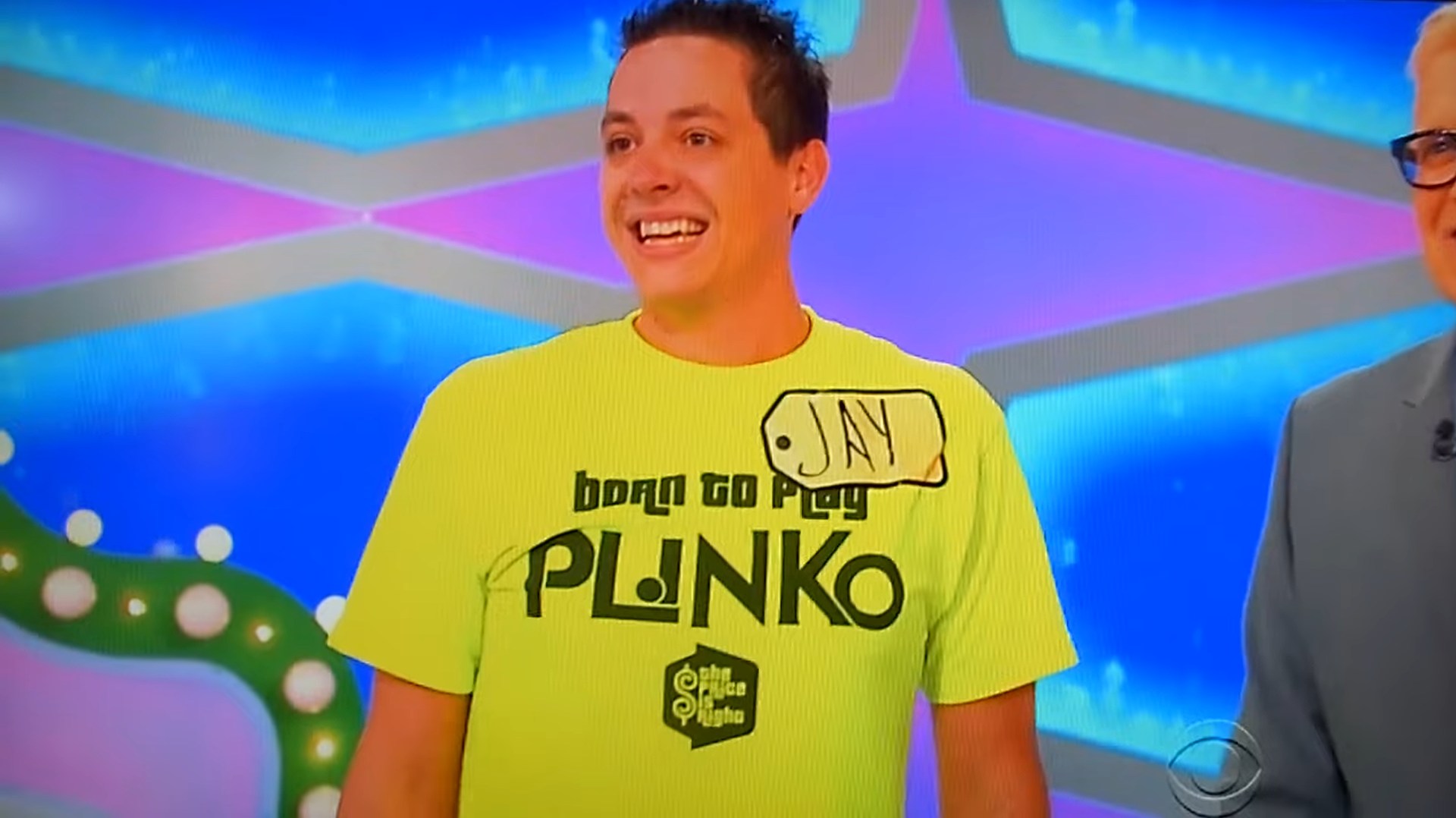 A contestant named Jay stands on stage wearing a bright yellow shirt with 'Born to Play PLINKO' printed on it, smiling as he interacts with the host of The Price is Right.
