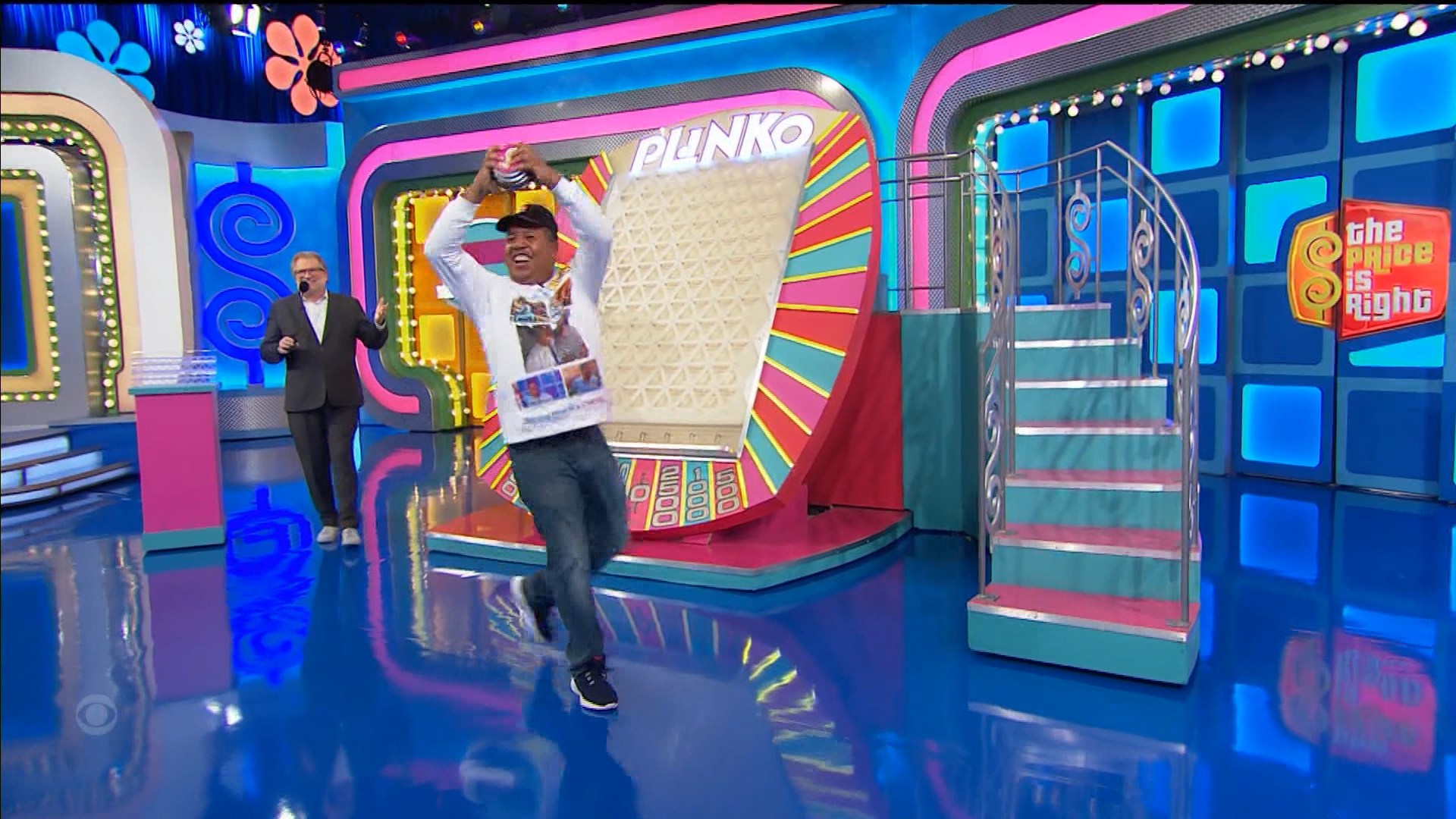 John reacts with joy after having won a stack of Plinko chips, which he shows off as he runs up the board to drop them.