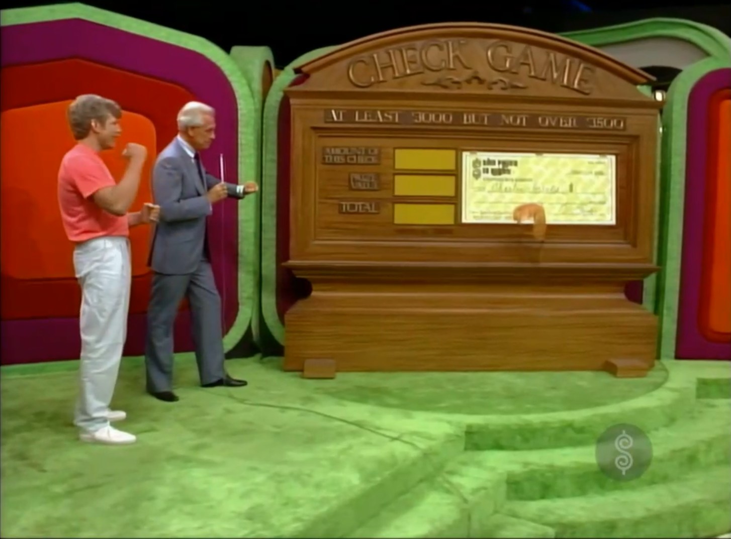 Contestants participating in a pricing game titled 'Check Game' featuring a large wooden display with sections showing the amount of the check, the prize value, and the total. One contestant is seen with his hand raised while the host points at the display.
