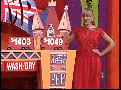 Janice Pennington playfully "bumps"  a colorful game display featuring two toy cars with price signs: 03 and 49, on a bright, festive background.