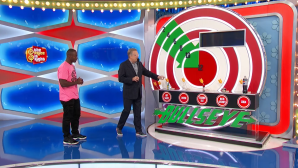 Drew Carey gestures towards a colorful game board labeled 'BULLSEYE' while a contestant stands beside him, both appearing on the set of The Price is Right.