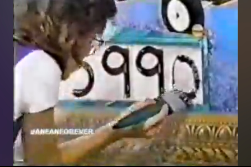 A Price is Right contestant using a paintbrush filling in a number on the Gallery Game display showing '5990'.