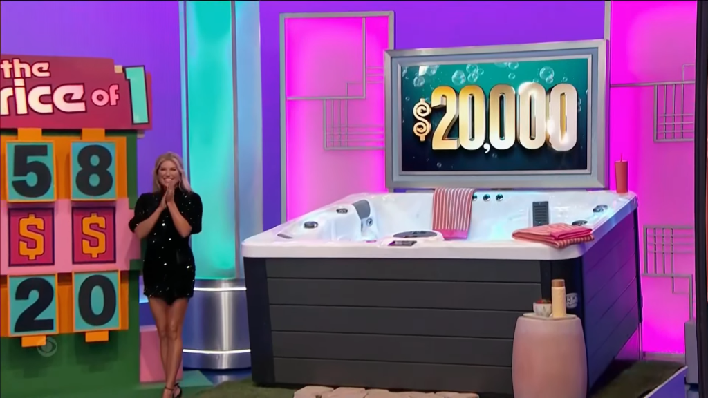 A model stands excitedly beside a hot tub on a game show set, with a large price tag of ,000 displayed in the background.