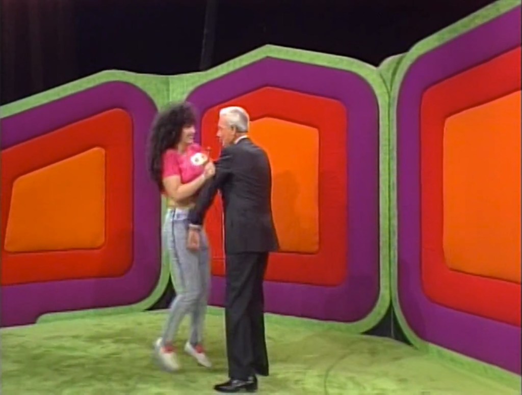 A woman named Marilyn in a pink shirt and jeans joyfully interacts with a man in a suit on a 1991 episode of The Price is Right.